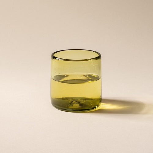 An olive green short transparent drinking glass, filled with water.