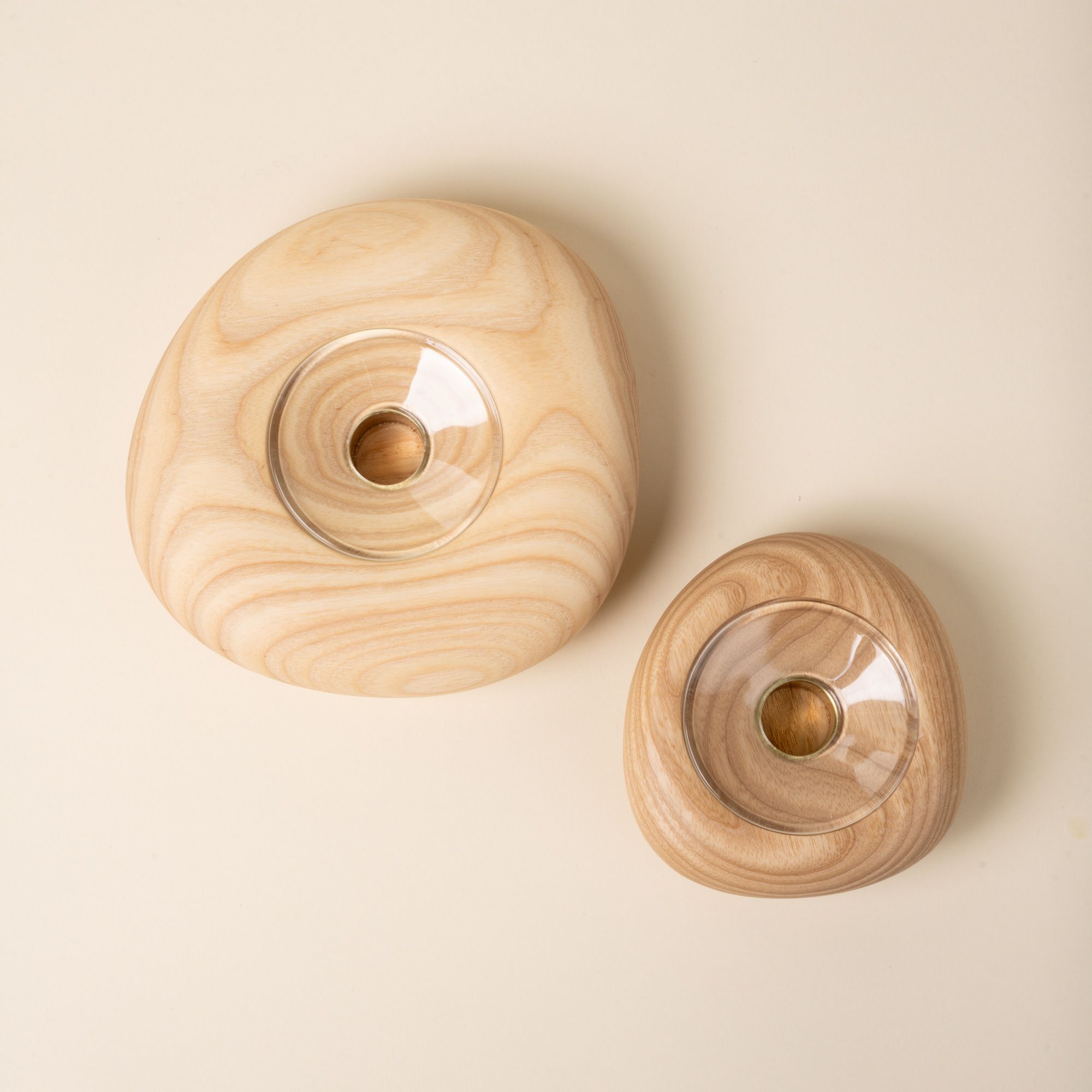 Top-down view of two round light wood candle holders in different sizes, each with a clear glass insert in the center, set against a neutral background.