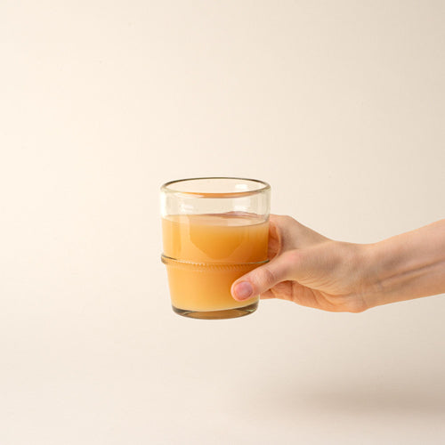 A clear short recycled glass tumbler with a ridged band detail, filled with iced coffee.