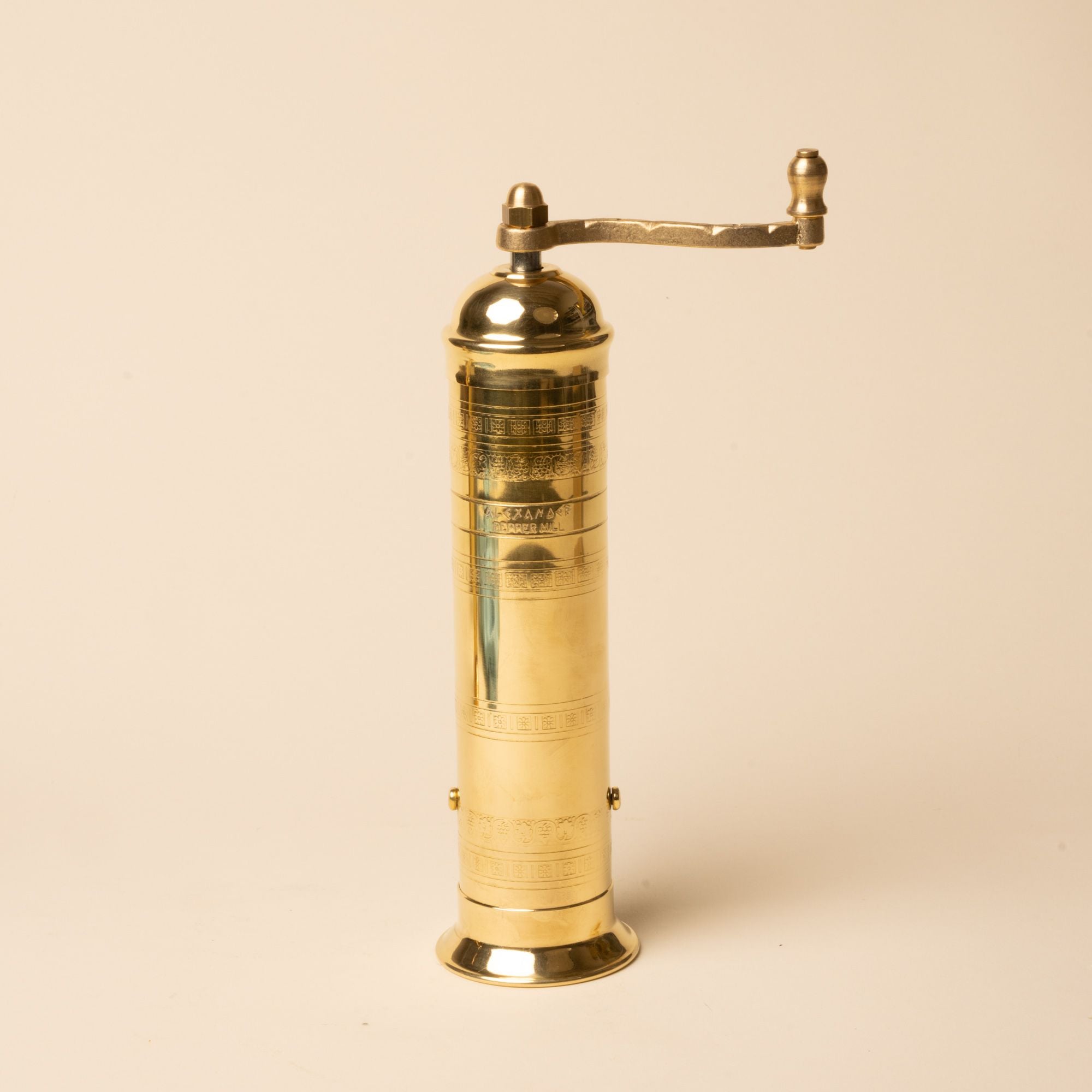 Brass hand-crank pepper grinder with engraved details, standing upright on a neutral background.