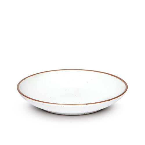 A large ceramic plate with a curved bowl edge in a cool white color featuring iron speckles and an unglazed rim.