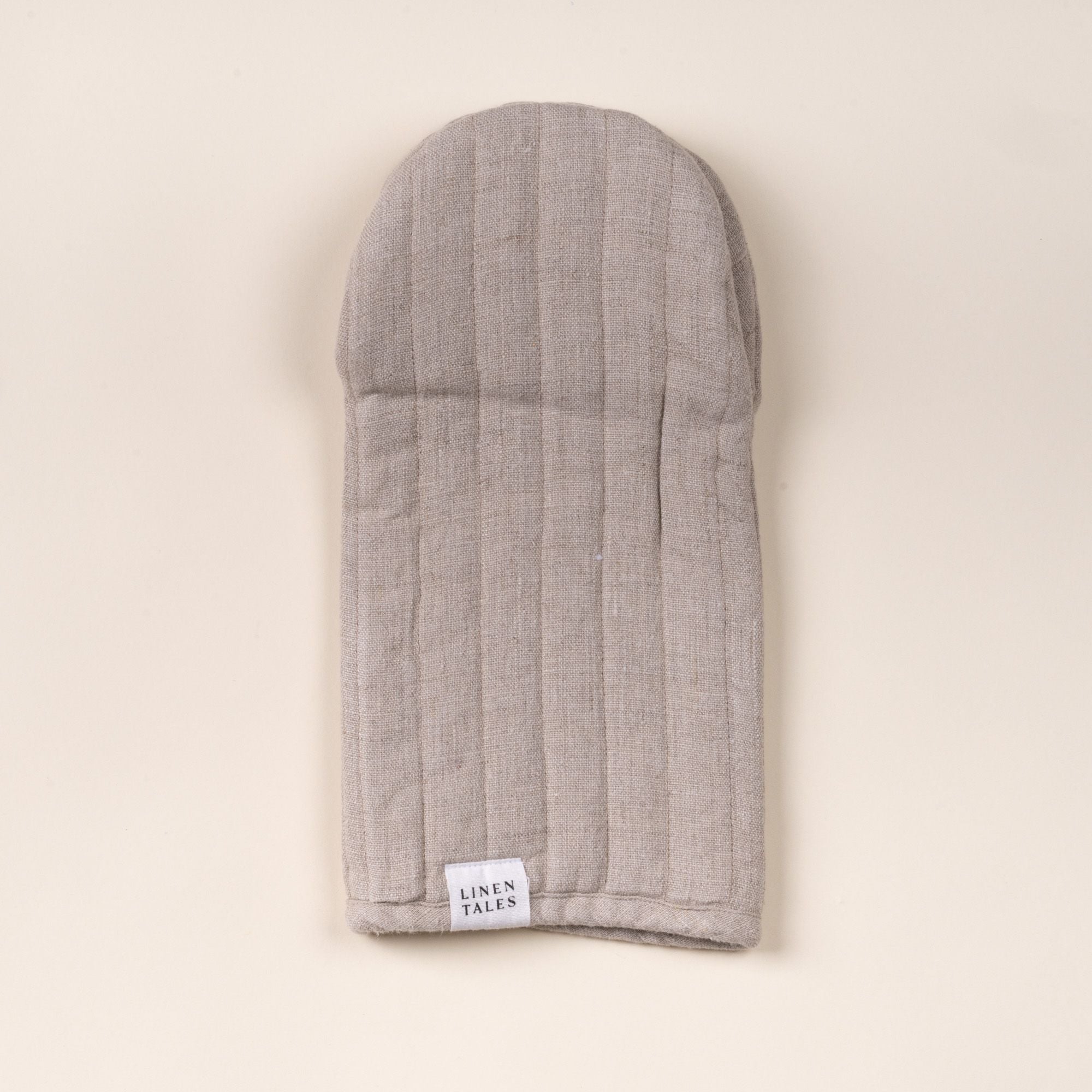 Natural color linen oven mitt with stitched channels and a small ‘Linen Tales’ label, laid flat on a light background.