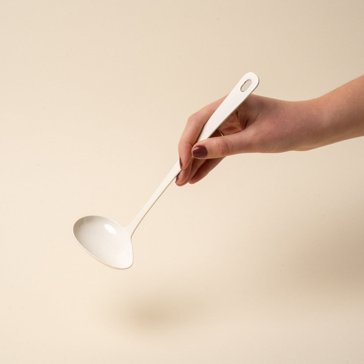 A hand hold a white enamel sauce ladle with a hole at the end of the handle for hanging