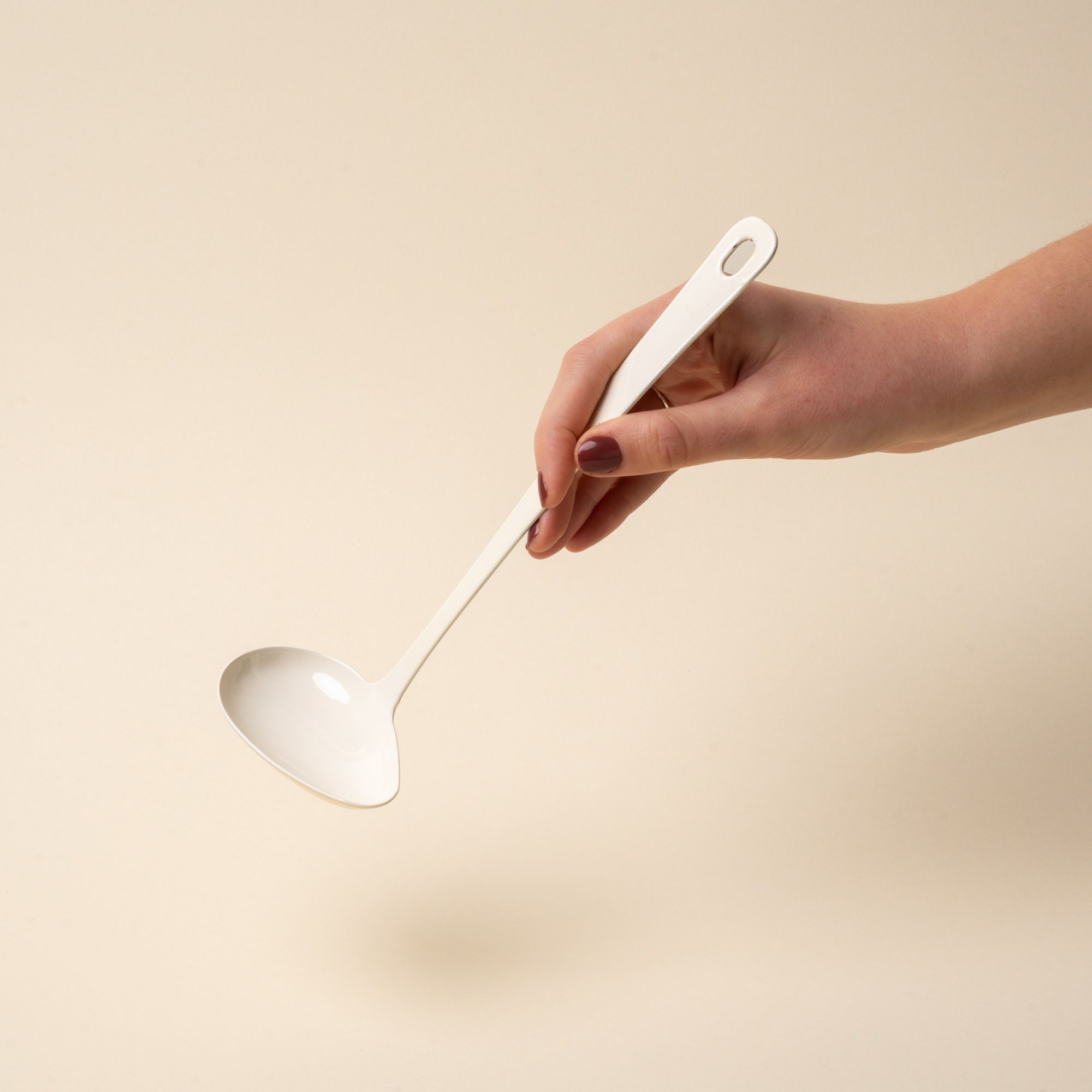 A hand hold a white enamel sauce ladle with a hole at the end of the handle for hanging