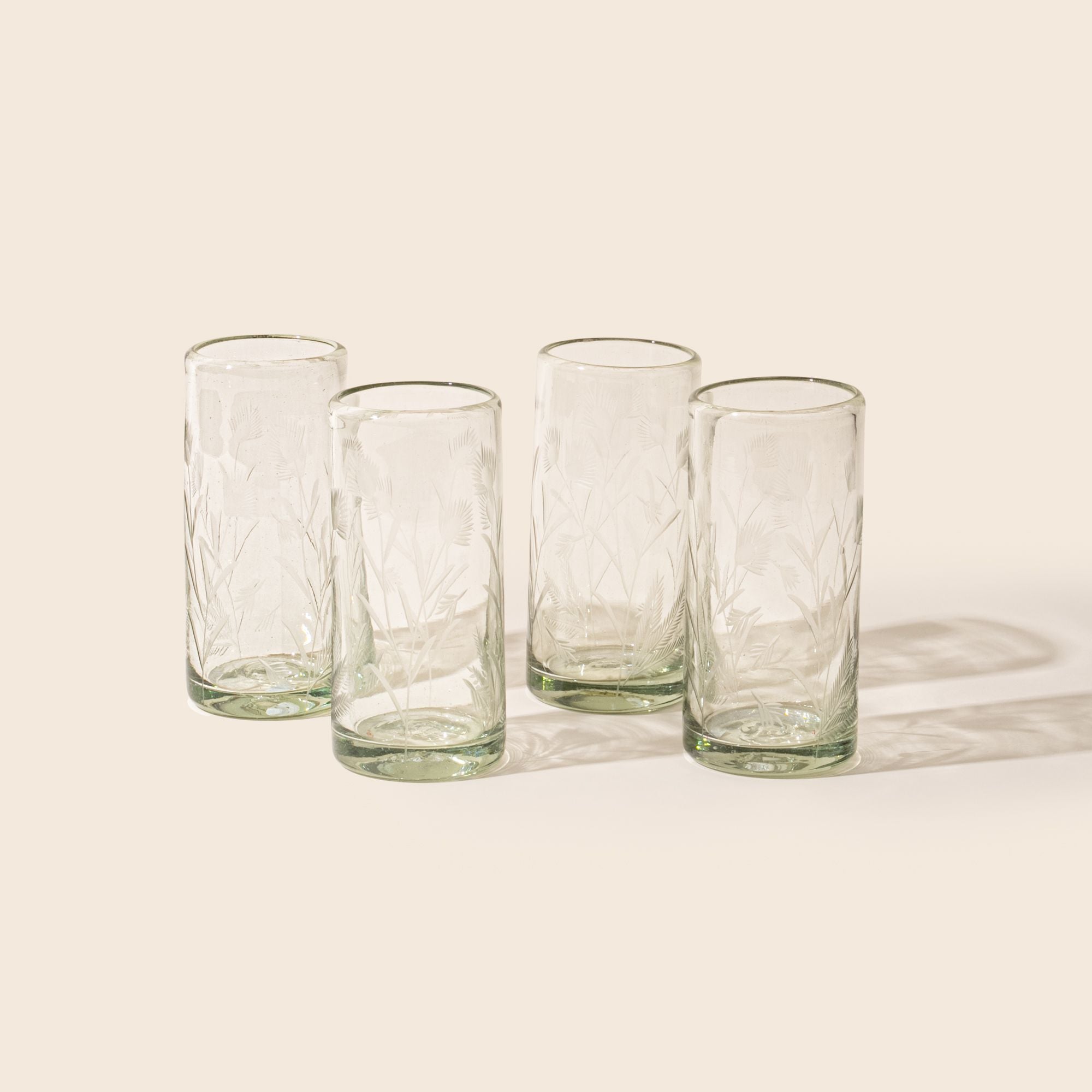 Four clear cylindrical glass with delicate etched floral pattern, standing upright on a neutral background.