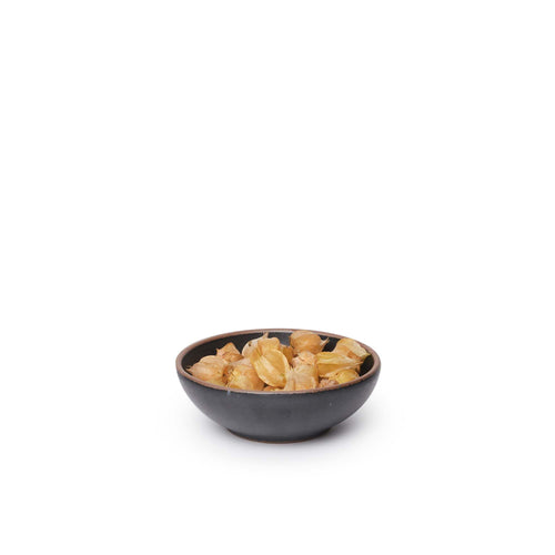 A small shallow ceramic bowl in a graphite black color featuring iron speckles and an unglazed rim, filled with food