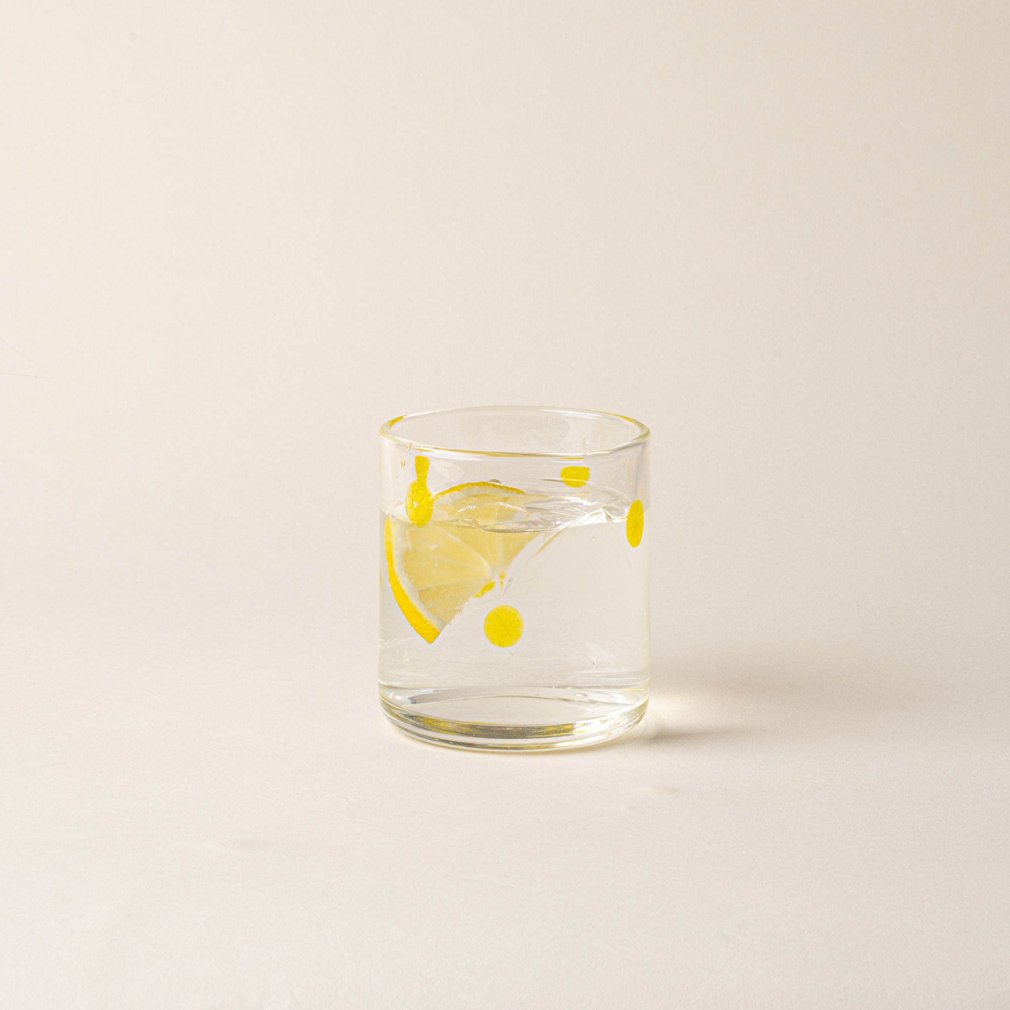 Clear glass tumbler with yellow lemon slice motif, filled with water and a lemon slice.