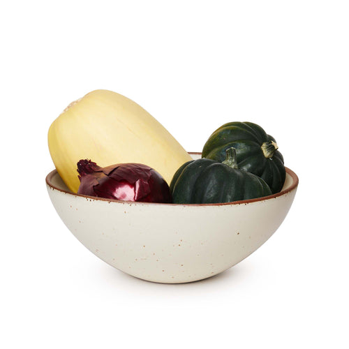 A large ceramic mixing bowl in a warm, tan-toned, off-white color featuring iron speckles and an unglazed rim, filled with a medley of vegetables