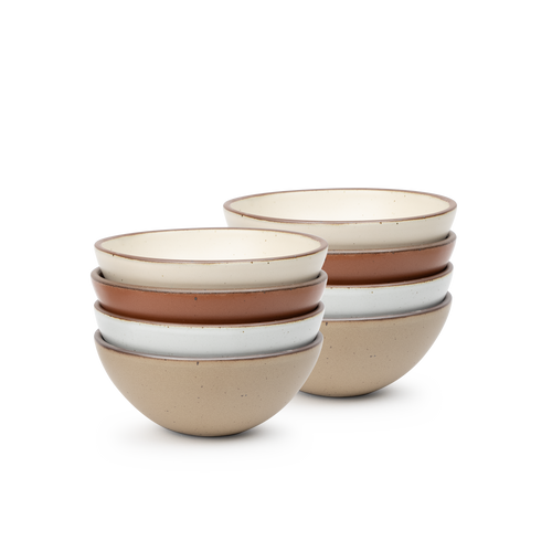 A stack of 8 medium sized rounded ceramic bowls in a cool terracotta, warm off-white cool white, and warm pale brown colors featuring iron speckles and an unglazed rim