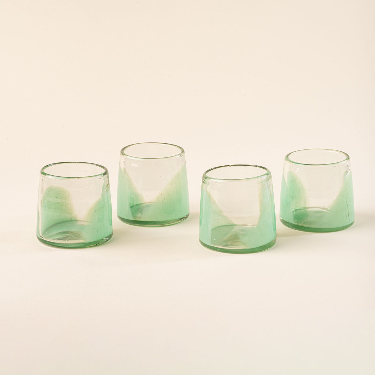 Four short clear glasses with pastel green arch bases arranged in a row on a light background.