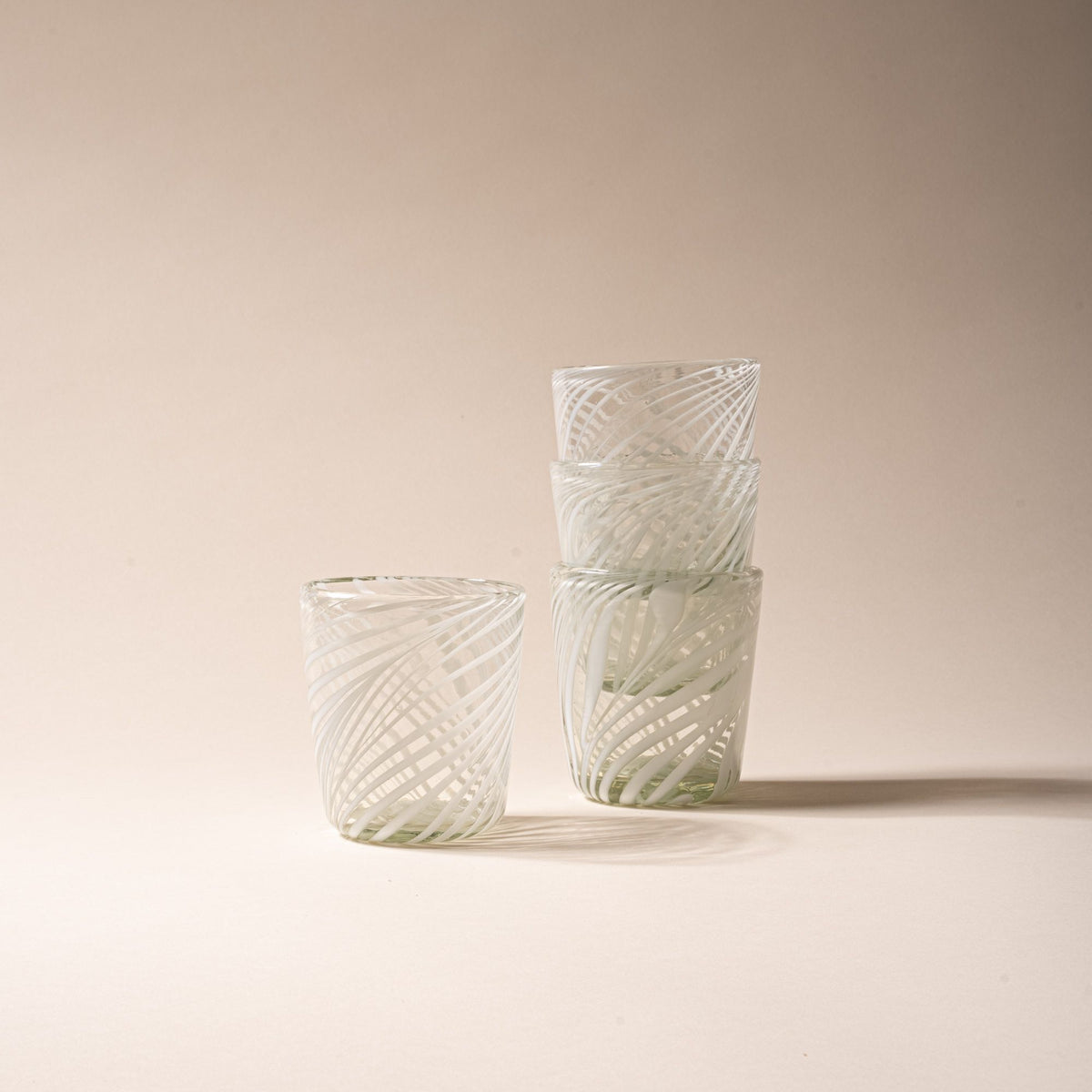 Set of four clear short tumblers with white swirling stripe design, three stacked and one standing beside on neutral backdrop.