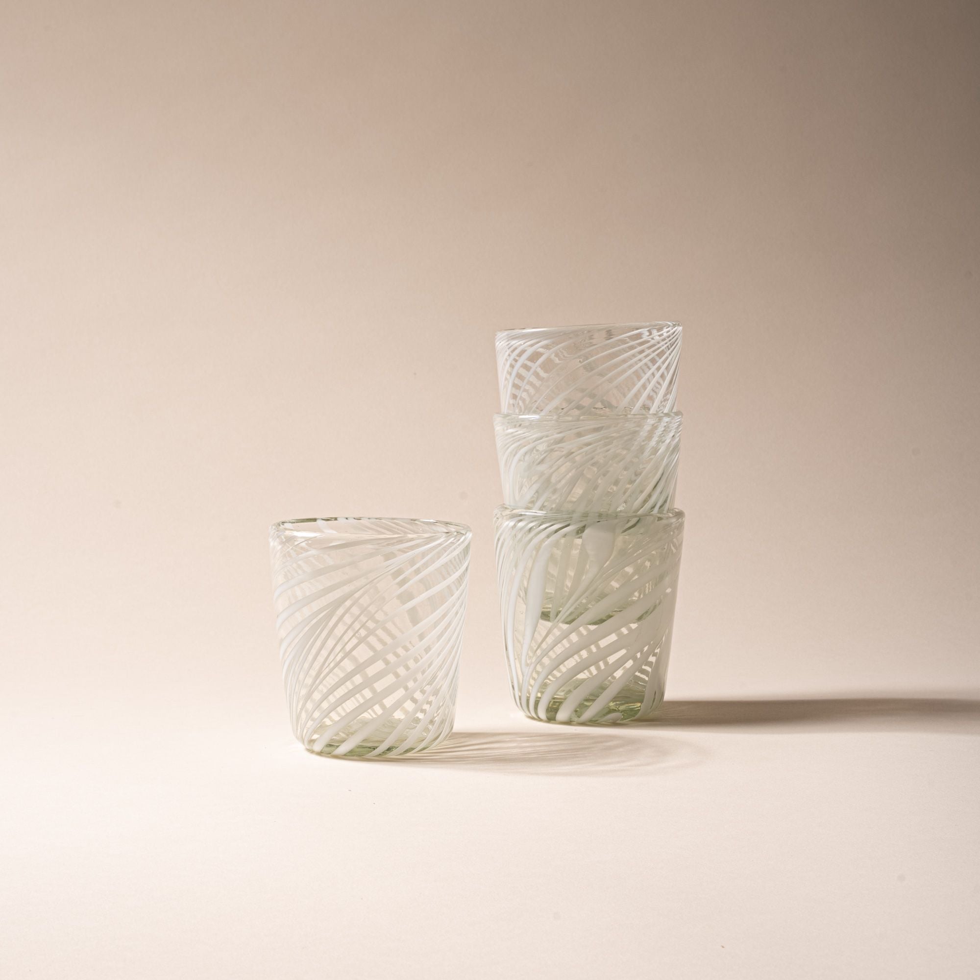Set of four clear short tumblers with white swirling stripe design, three stacked and one standing beside on neutral backdrop.