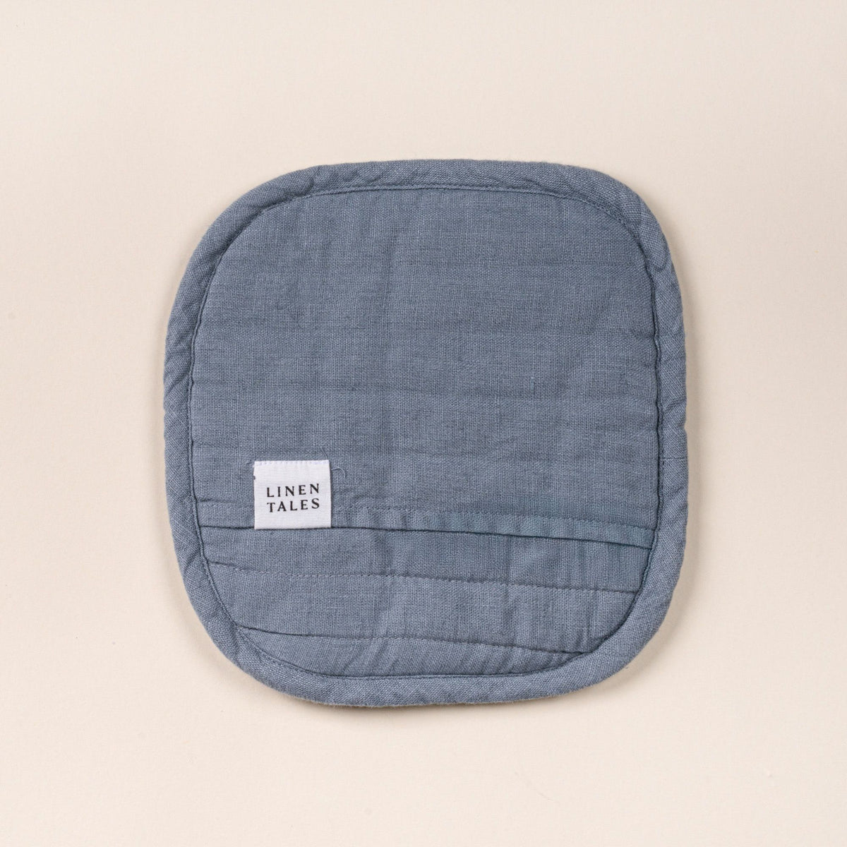 Square quilted linen potholder in a blue-grey color with rounded corners and a small ‘LINEN TALES’ label, on a light background.