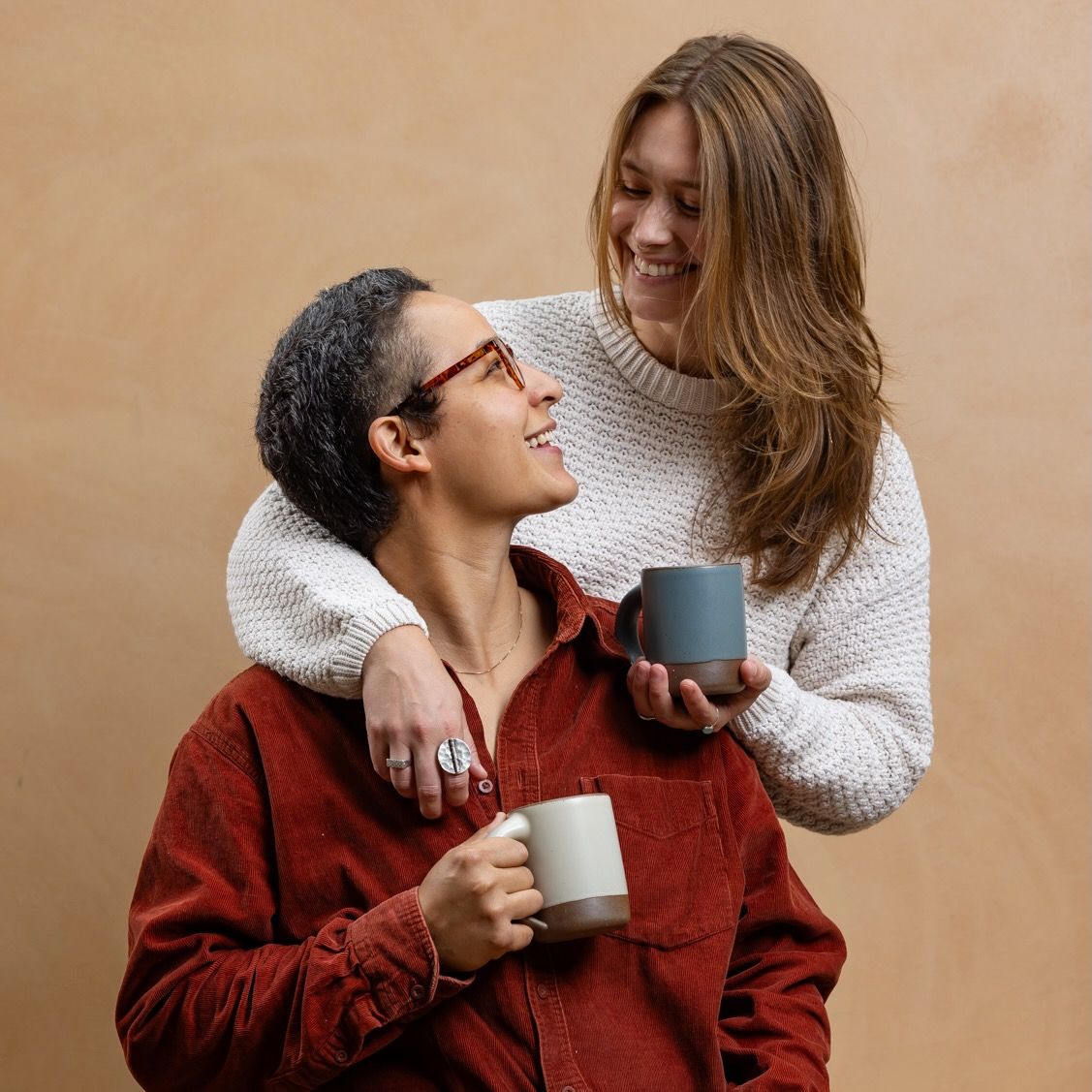 A couple is smiling and staring at each other, each holding a ceramic mug in a blue-grey or icy white color.