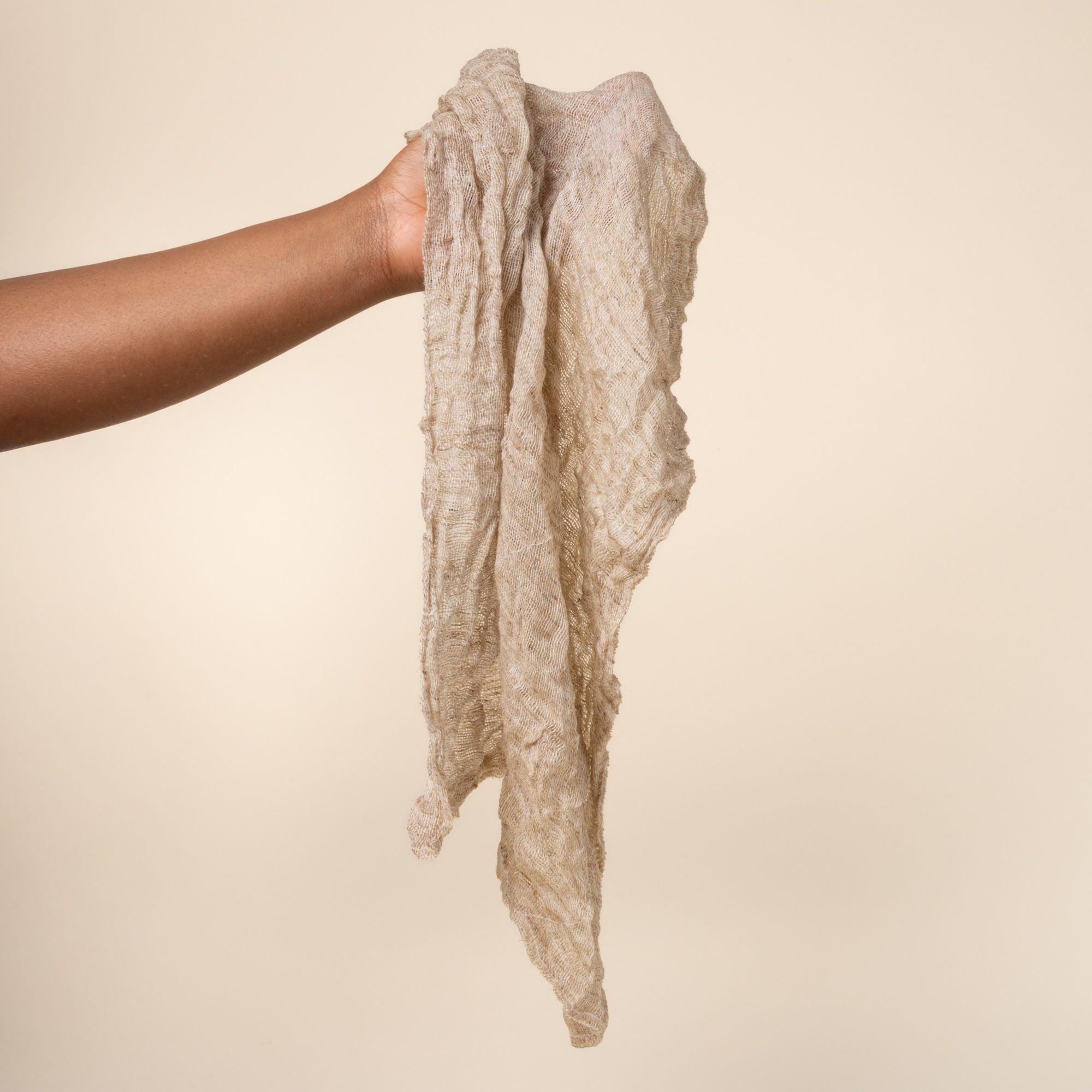 Hand holding a loose and wet natural linen cleaning cloth showing a subtle woven texture and stitched edges.