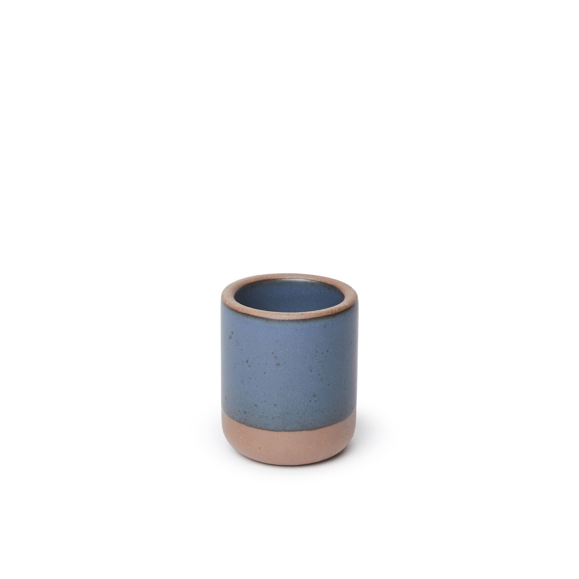A small, short ceramic mug cup in a cool, medium blue color featuring iron speckles and unglazed rim and bottom base, filled with milk.