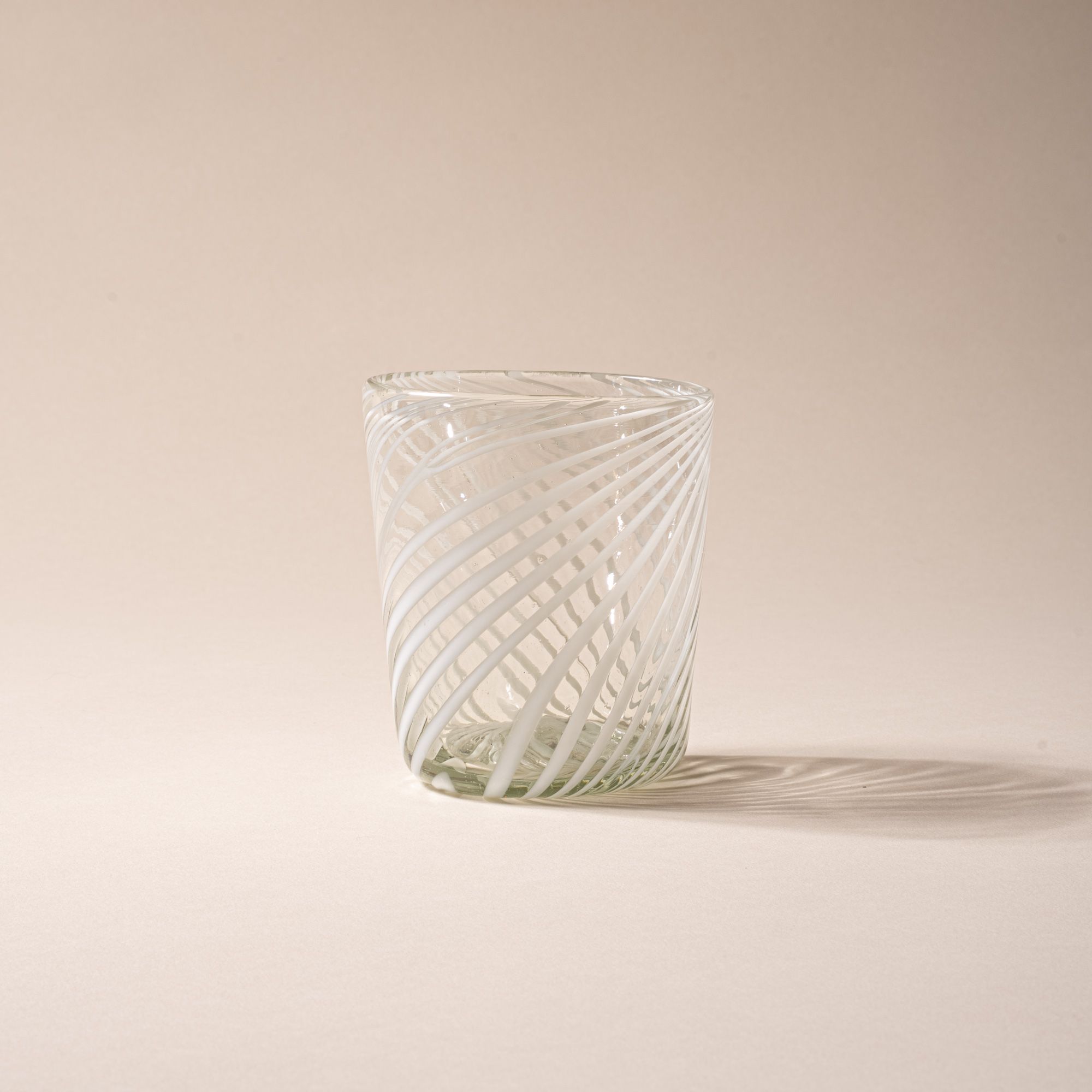 Clear glass tumbler with white diagonal swirl pattern against a neutral background.