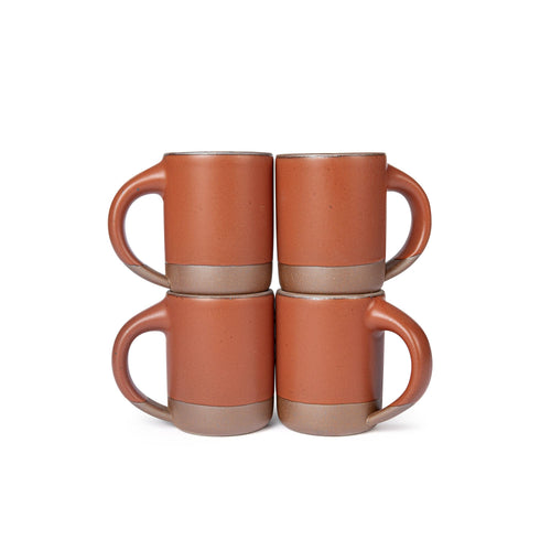 Four medium sized ceramic mugs with handles in a cool burnt terracotta color featuring iron speckles and unglazed rim and bottom base, stacked in sets of 2.