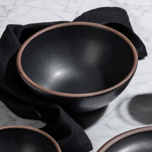 A medium rounded bowl in a graphite color with unglazed rim and a dinner napkin also in graphite.