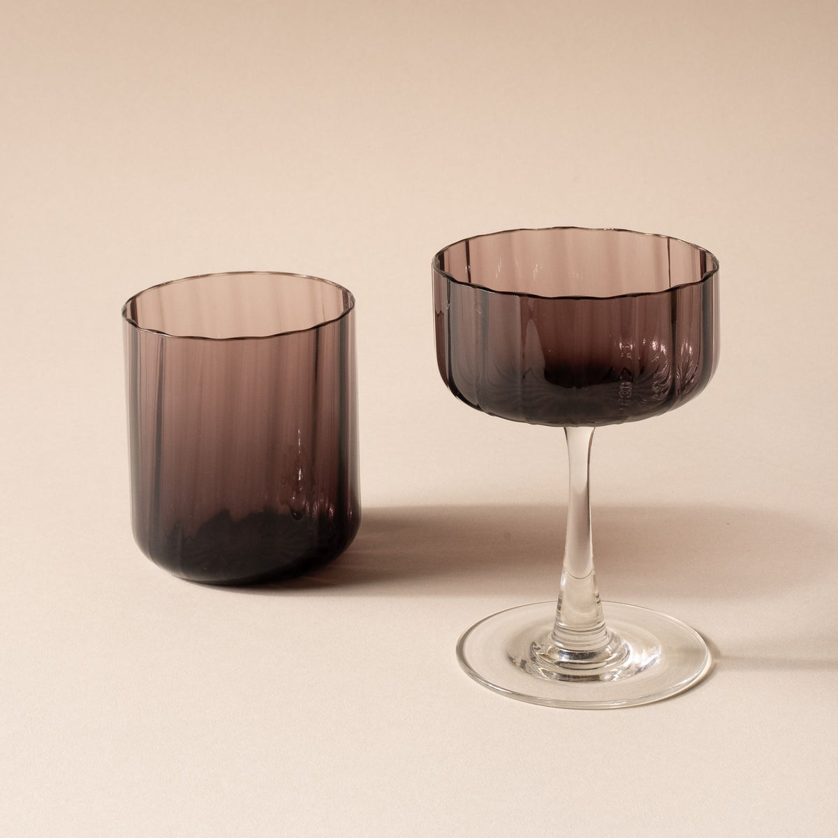 Cocktails in a fluted walled tumbler and coupe glass with a fluted bowl that is a grey purple color with a clear stem