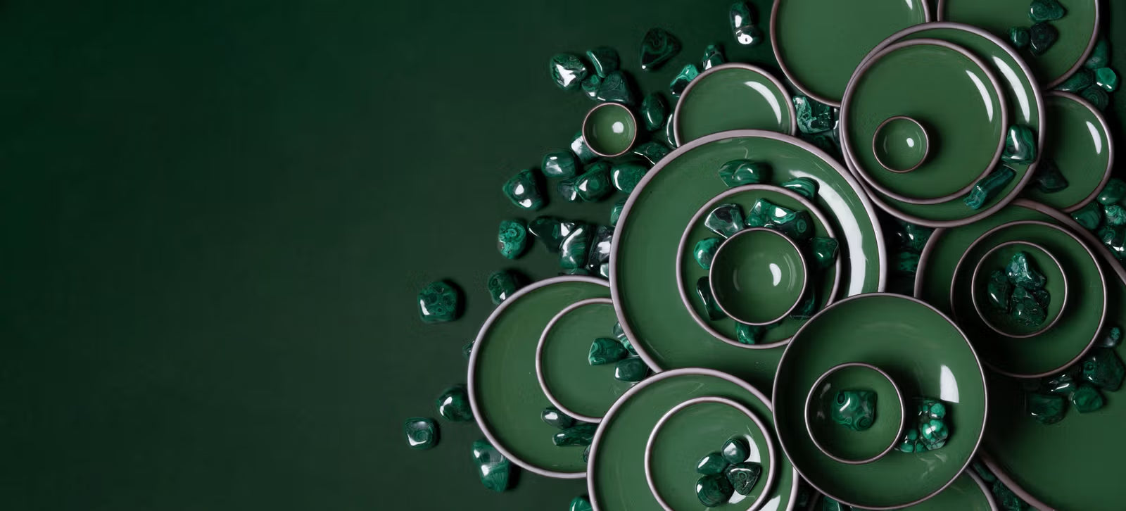 A collection of green ceramic bowls and plates arranged on a matching green surface, surrounded by polished green stones.