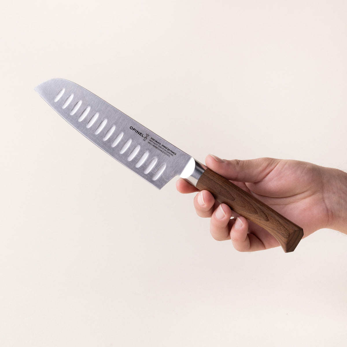 A hand holds a santoku knife with a sharp steel blade with dimples and a beveled dark wood handle