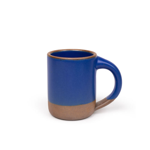 A medium sized ceramic mug with handle in a cobalt blue color featuring iron speckles and unglazed rim and bottom base.