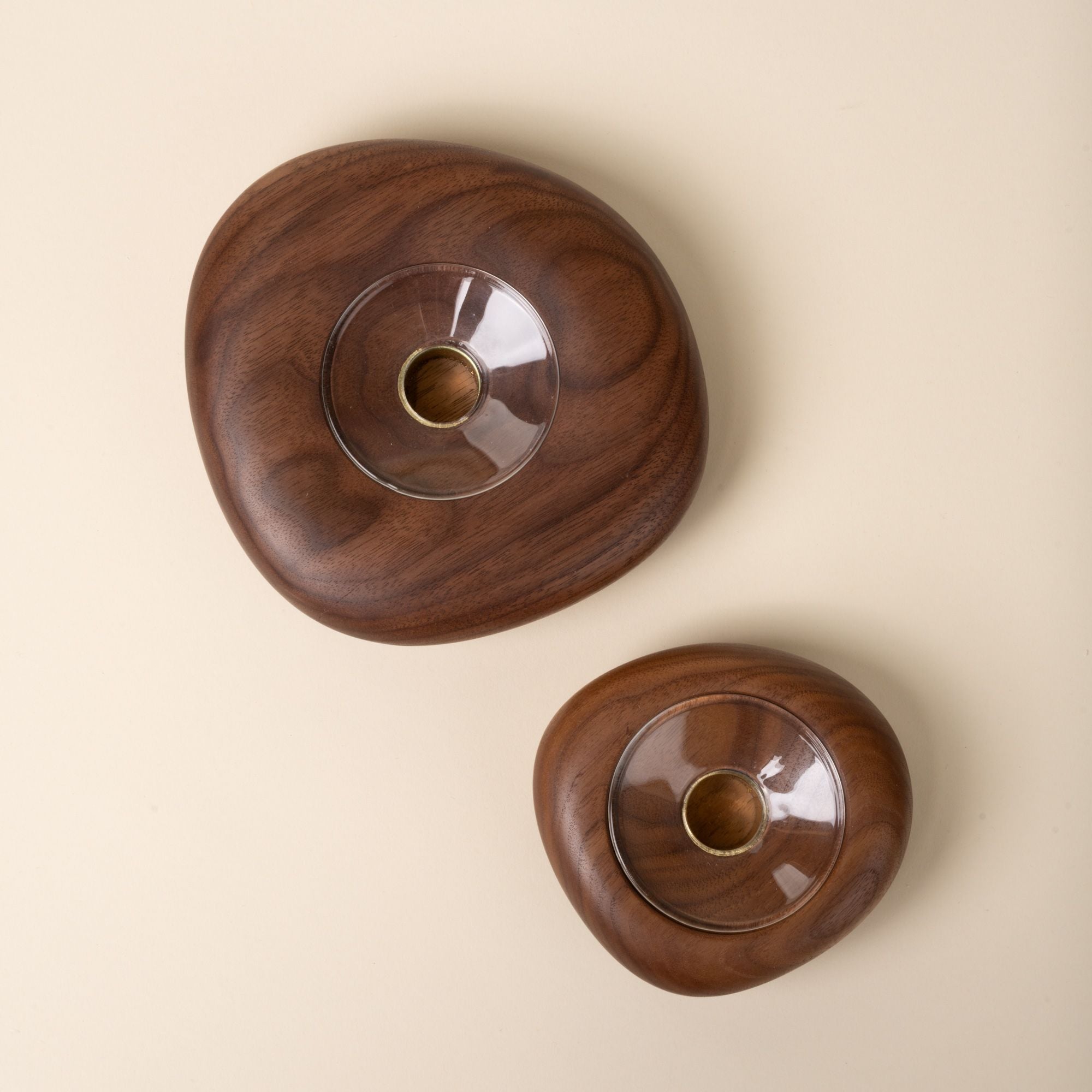Top-down view of two round walnut wood candle holders in different sizes, each with a clear glass insert in the center, set against a neutral background.