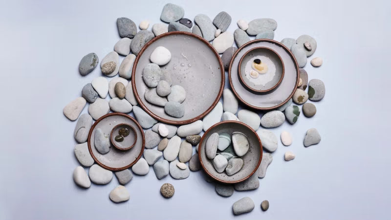 An artful arrangement of plates and bowls in a light gray color surrounded by rocks in similar hues.