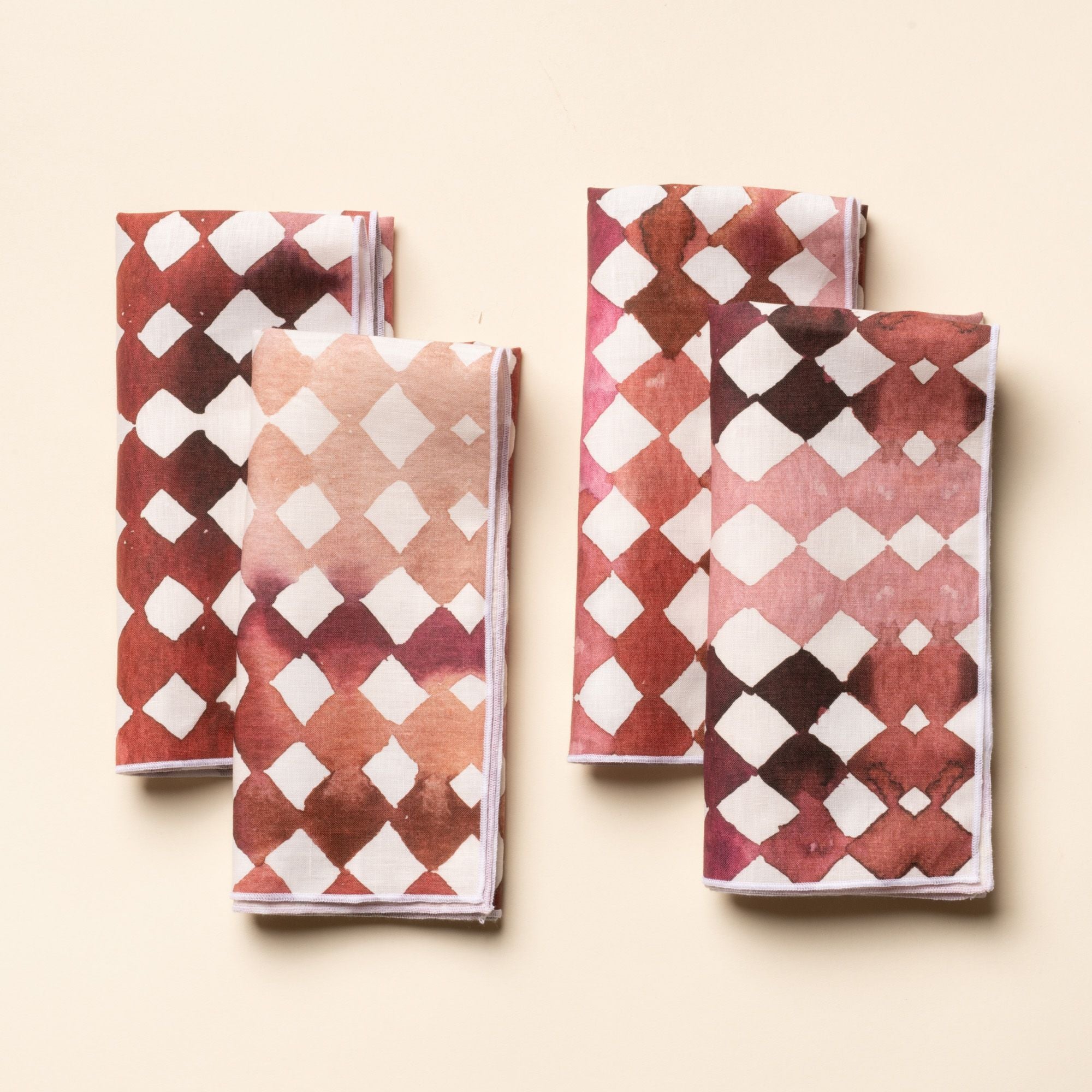 Set of folded watercolor diamond-patterned cloth napkins in warm burgundy and pink tones