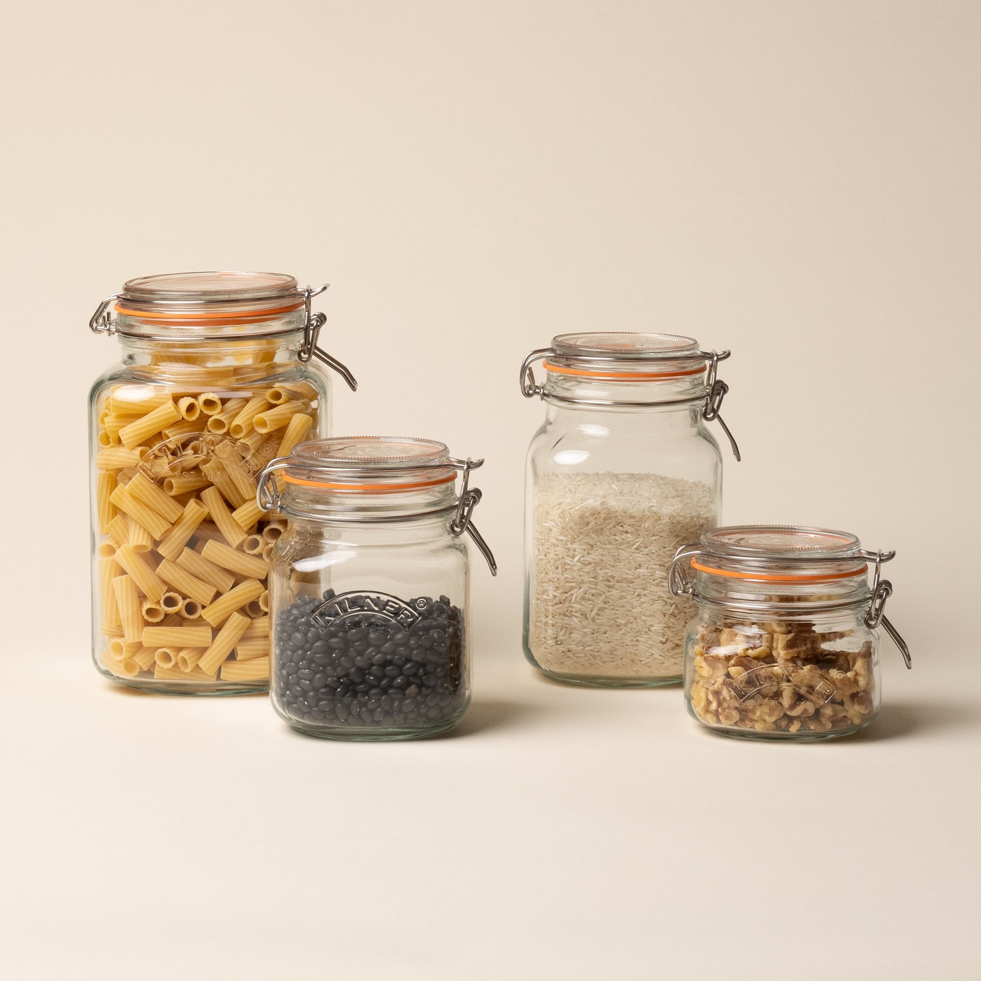 4 storage glass square jars filled with dried goods, in a row of largest to smallest, each topped with a lid with a rubber seal and steel clip closure.