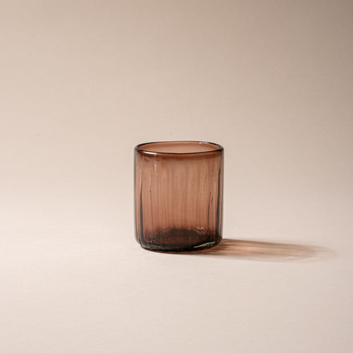 Amber-brown glass tumbler with vertical ridges, set against a neutral background.