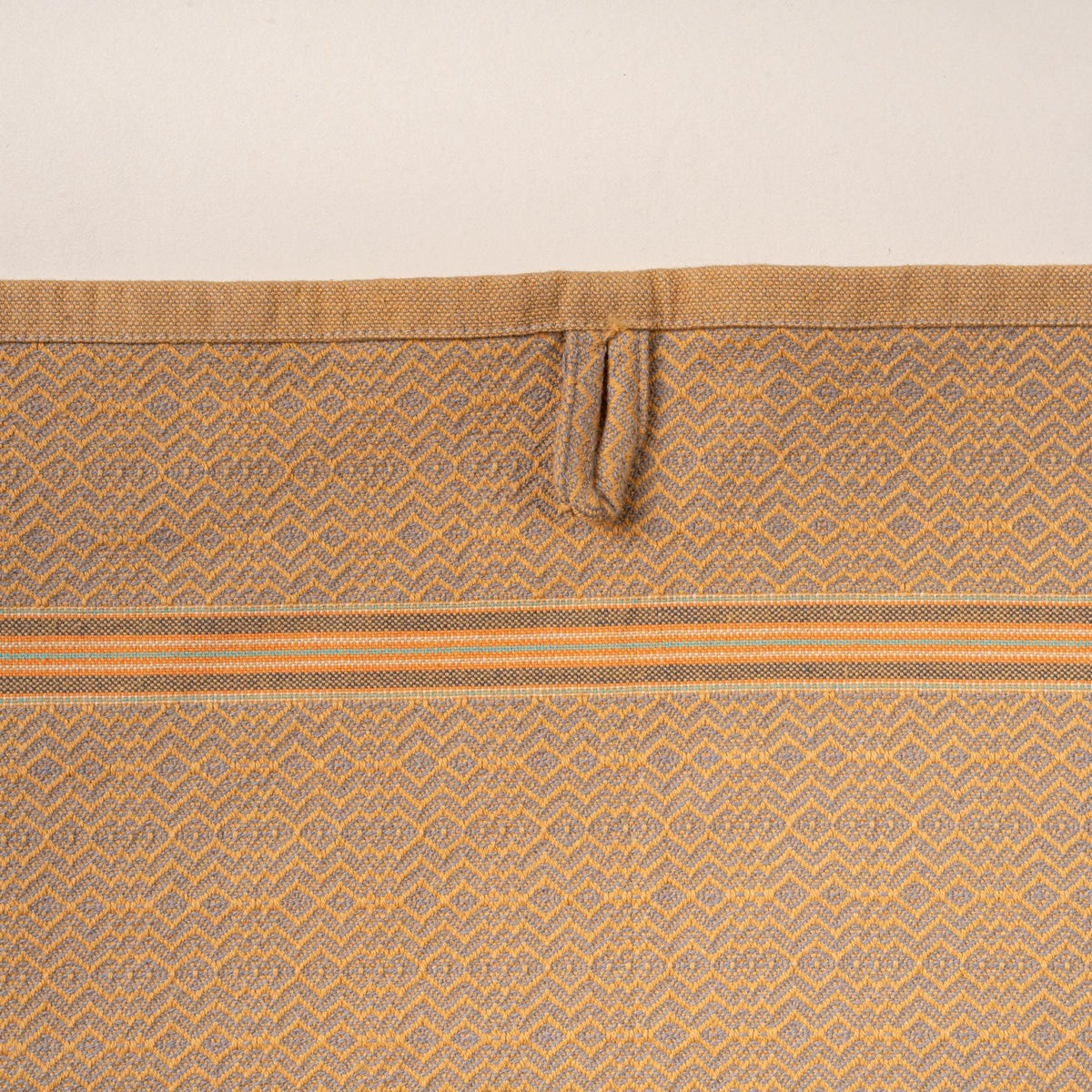 Close-up of a muted gold woven towel with a zigzag-and-diamond texture, stitched hanging loop, and thin striped band detail.