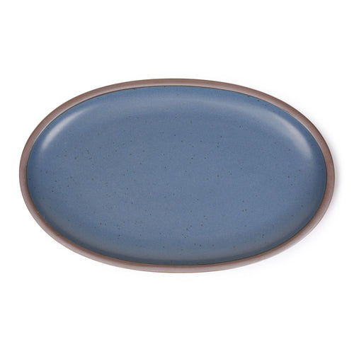 A large oval ceramic platter in a natural medium blue color featuring iron speckles and an unglazed rim