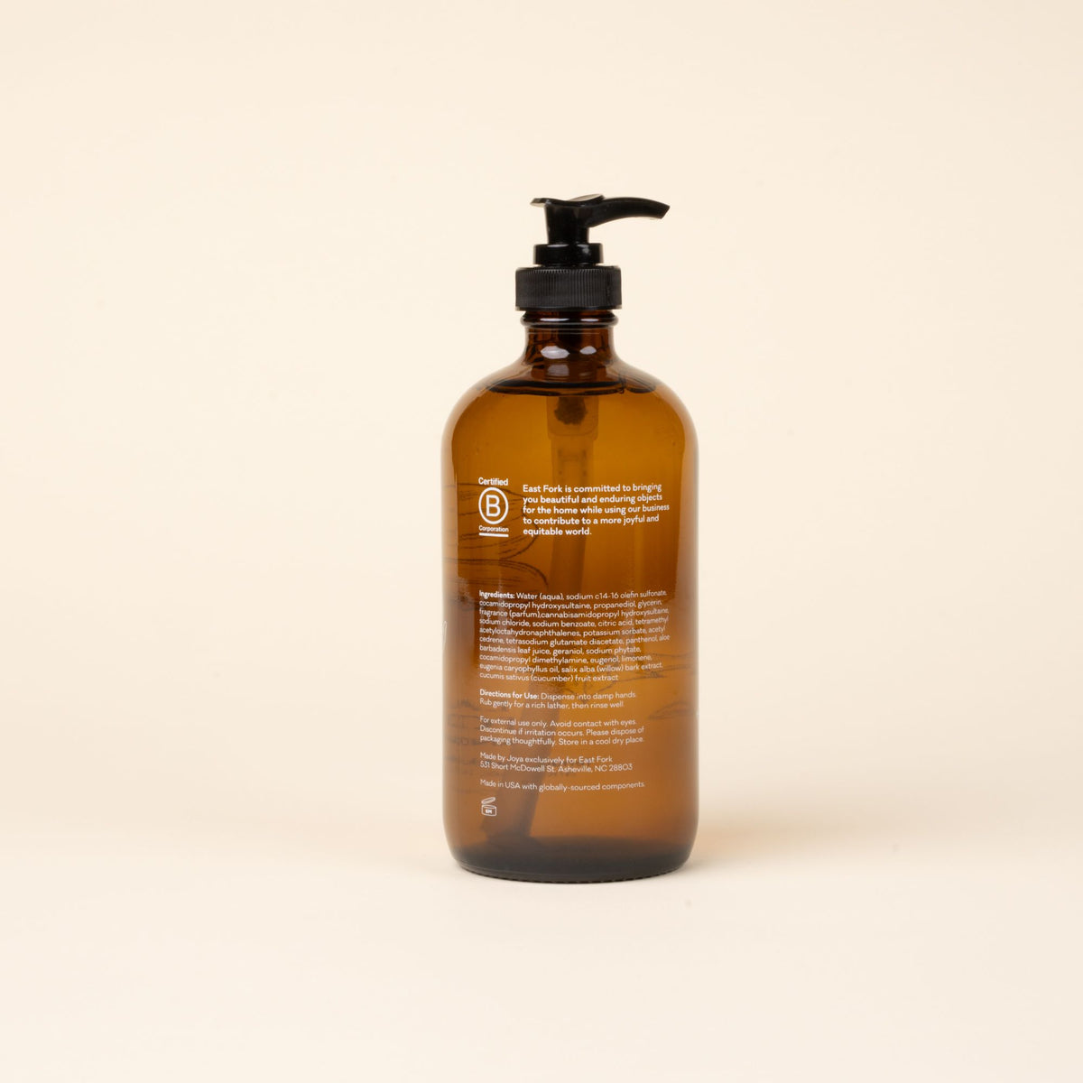 Back of amber glass pump bottle of East Fork hand soap with ingredients, centered against a light neutral background.