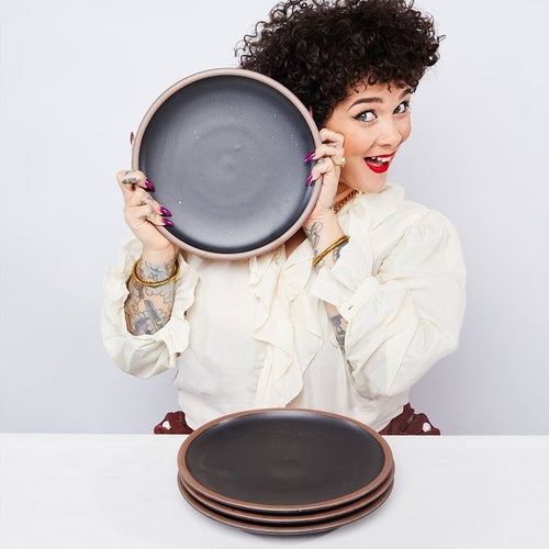 A person is smiling holding up a ceramic black dinner plate to their face.
