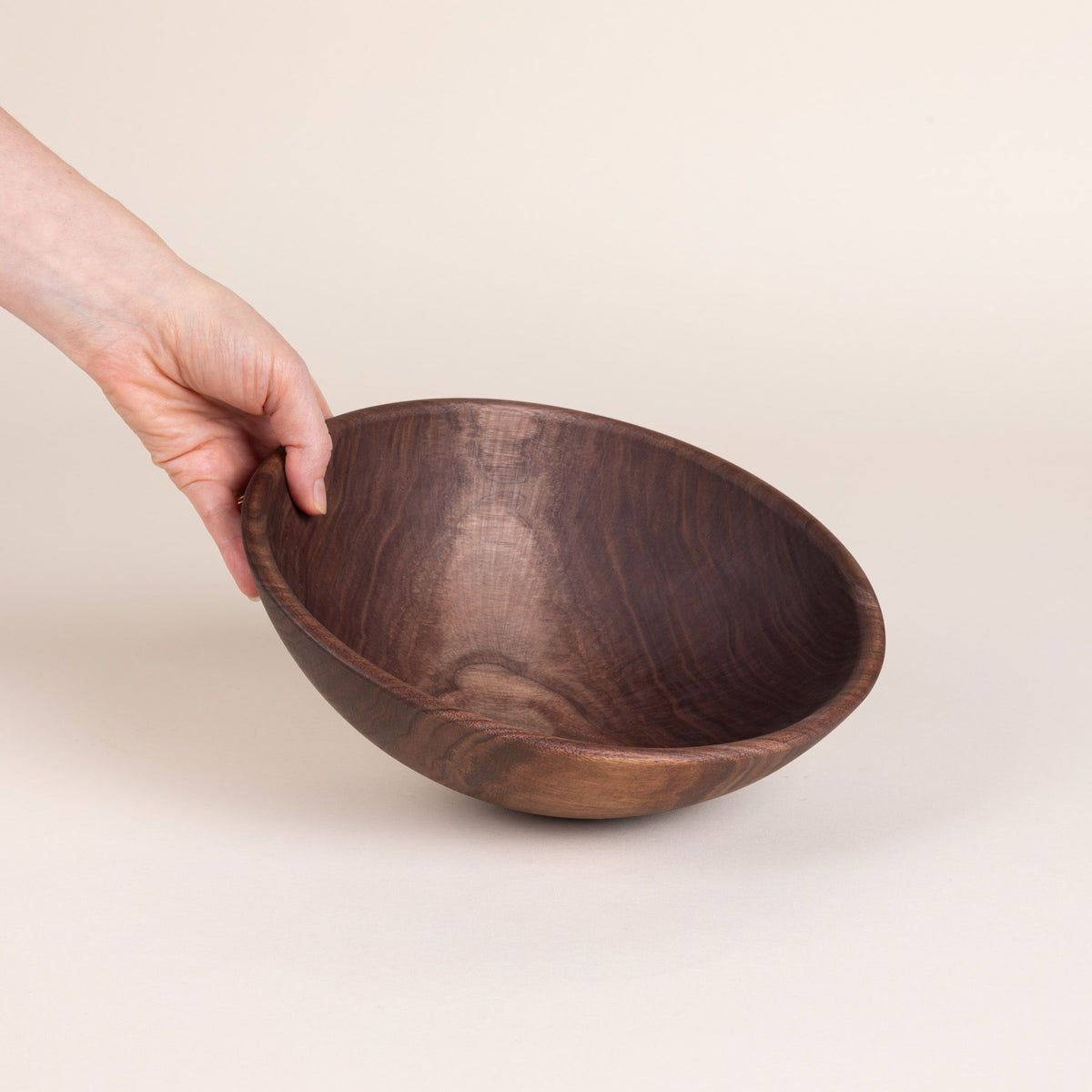 A hand holds out a medium walnut wood bowl