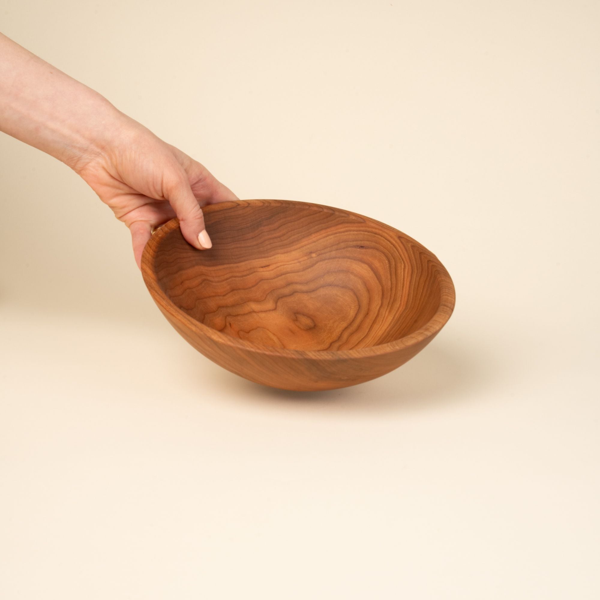 A hand holds out a medium sized round cherry wood bowl
