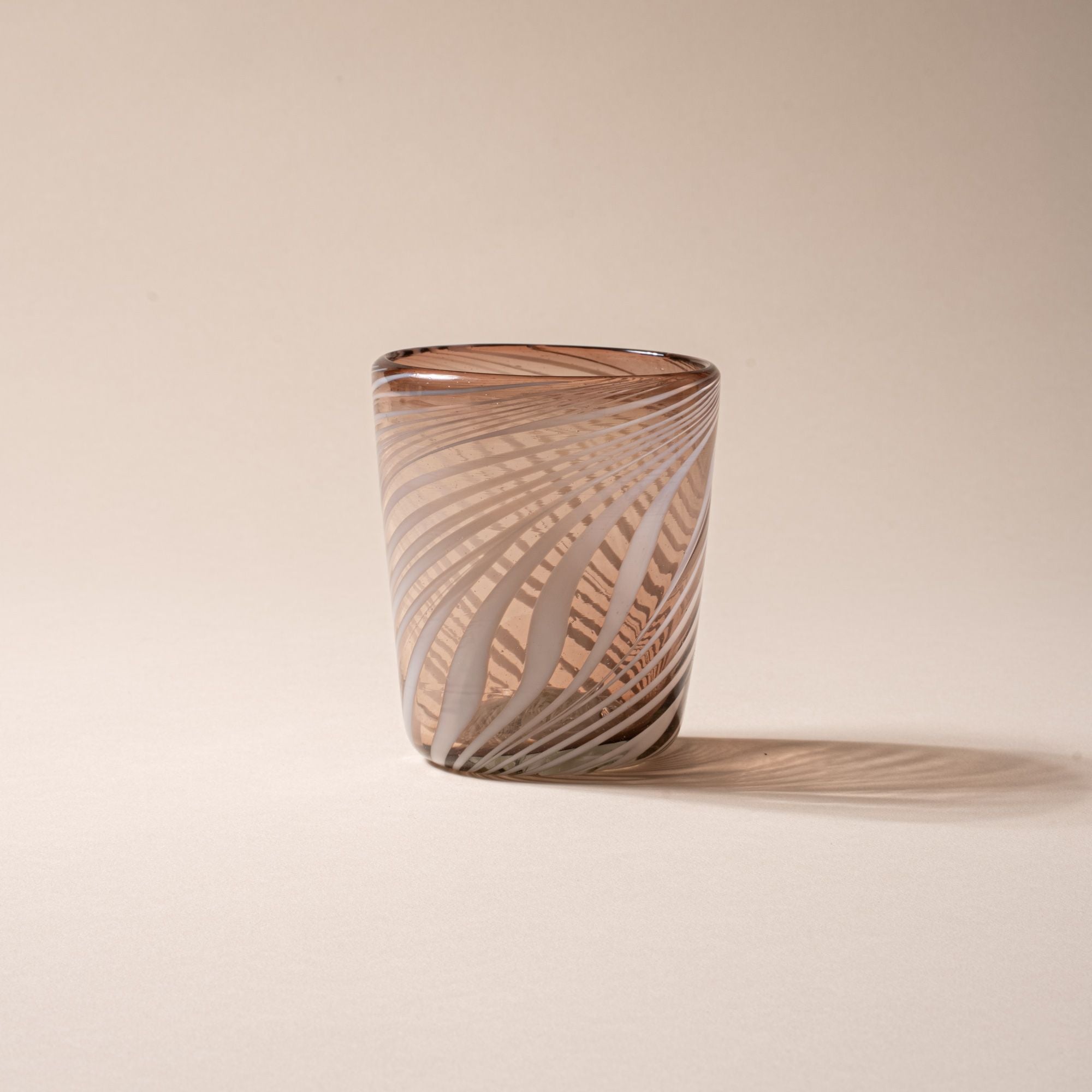 Smoky brown glass tumbler with white diagonal swirl pattern on a neutral background.