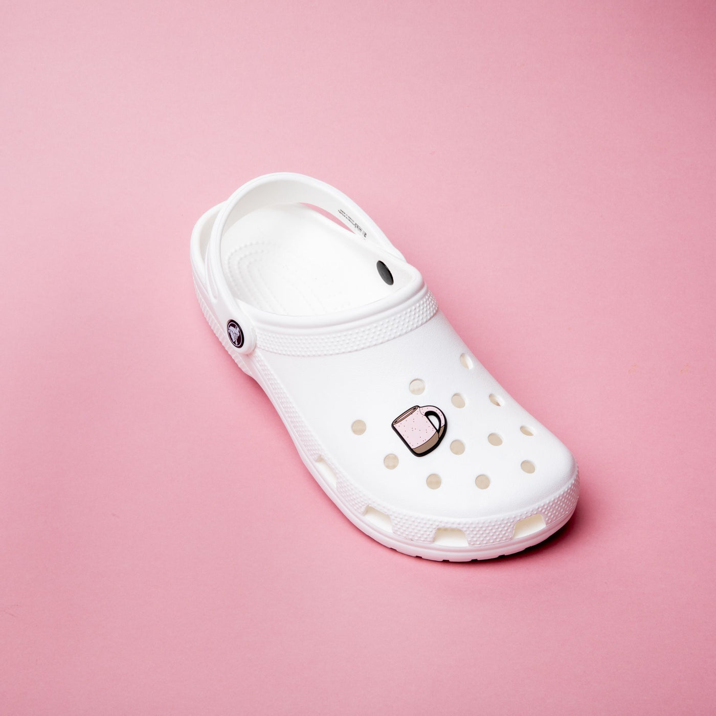Two feet with Crocs with The Mug charm on it