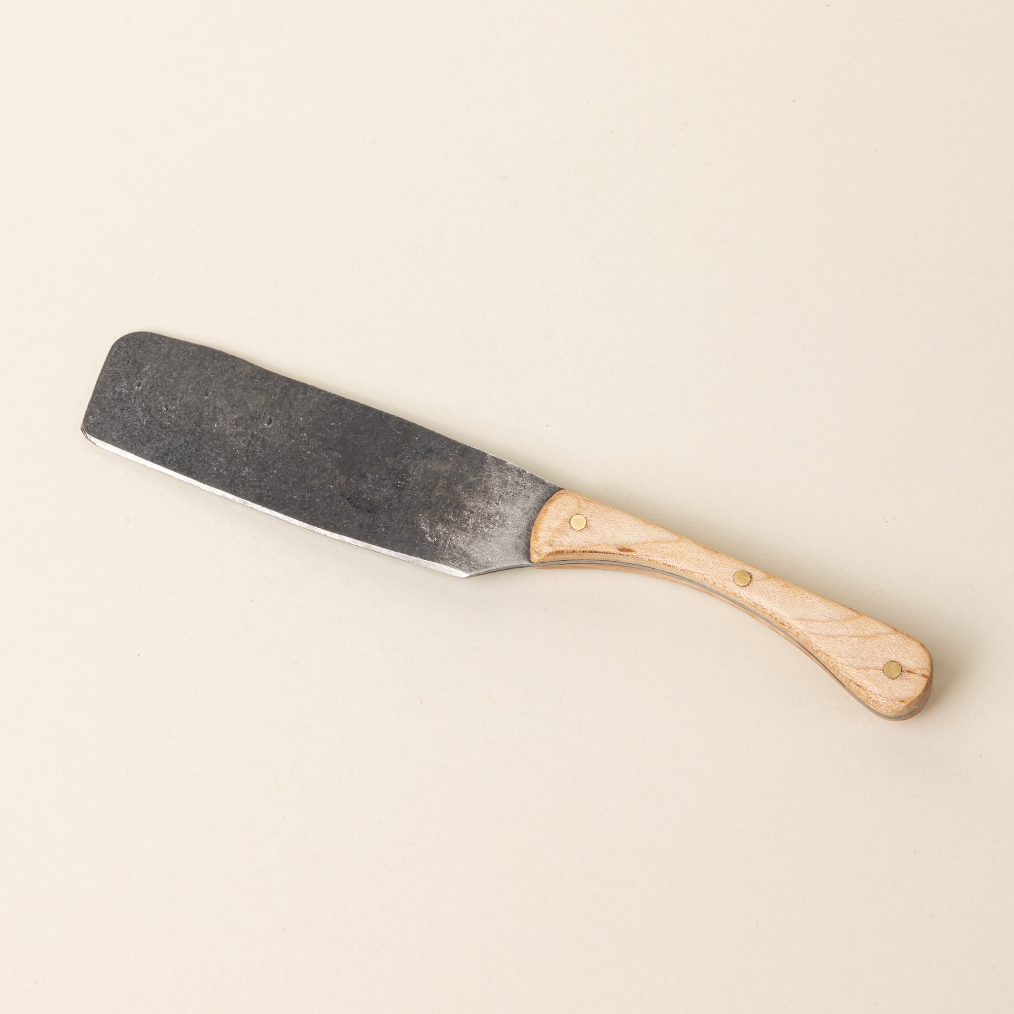 A hand-forged cheese knife with a stainless steel rectangular blade and a maple wood handle