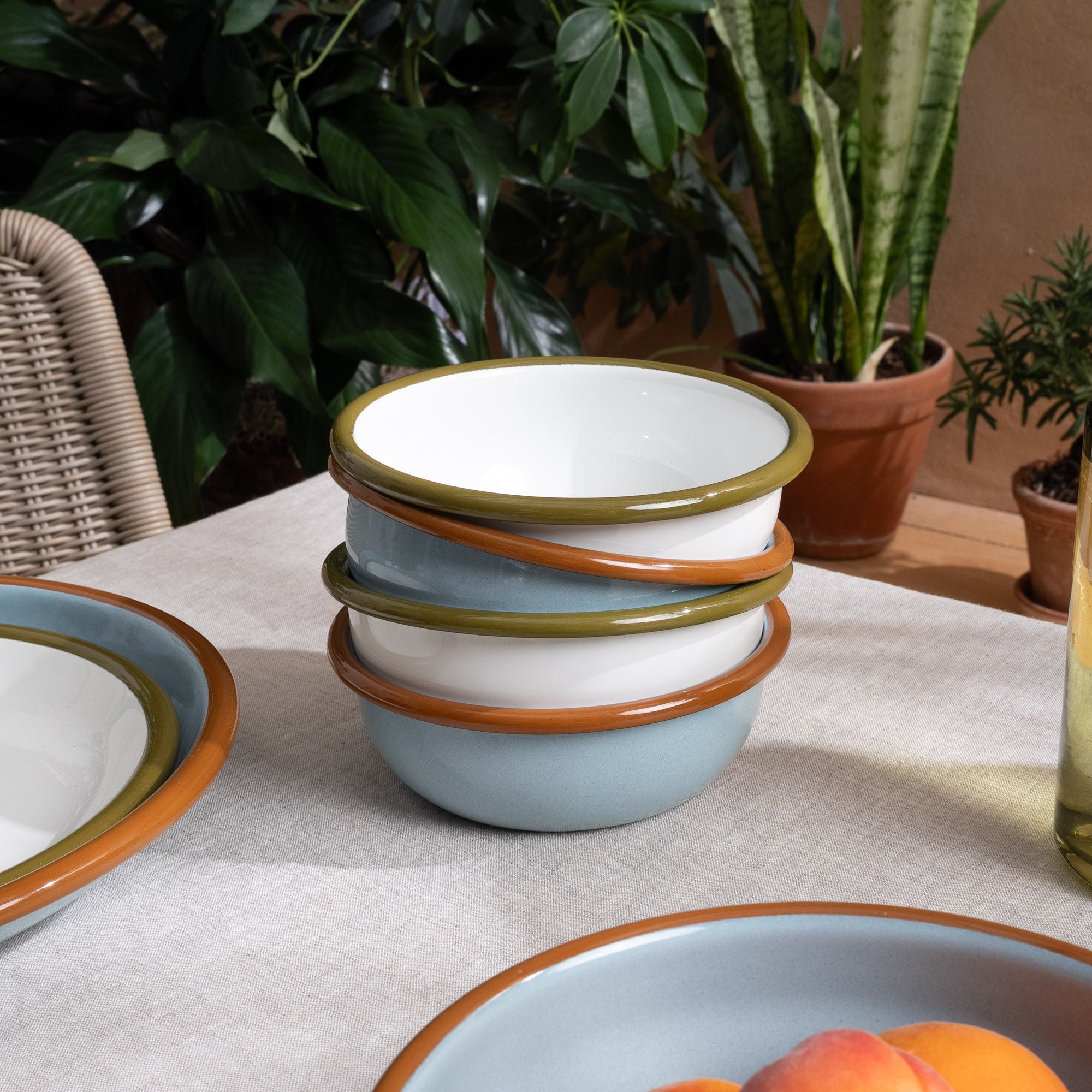 A stack of small enamel bowls in white and robin's egg blue on a table with more enamel dinnerware.