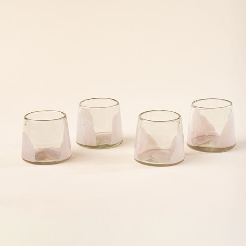 Four short clear glasses with pale light pink arch bases arranged in a row on a light background.