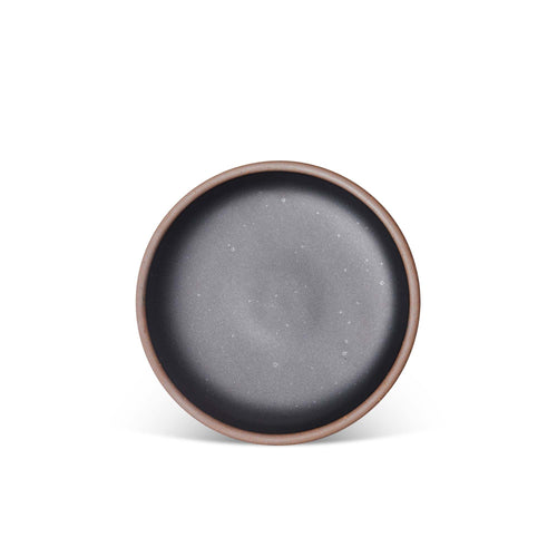 A medium sized ceramic plate in a graphite black color featuring iron speckles and an unglazed rim.