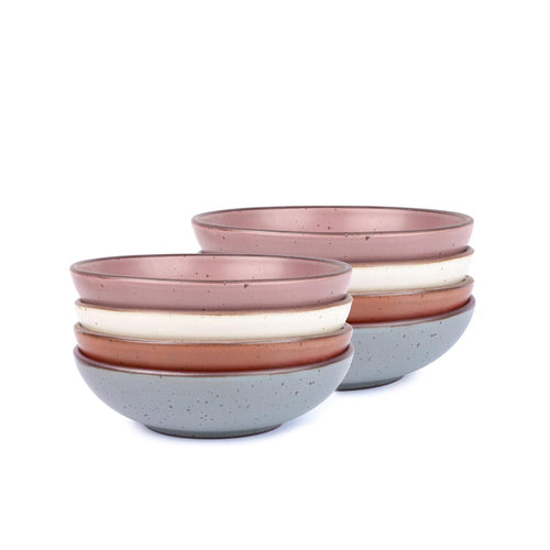 A stack of 8 dinner-sized shallow ceramic bowls in a warm off-white, cool terracotta, blue-grey and dusty mauve pink colors featuring iron speckles and an unglazed rim