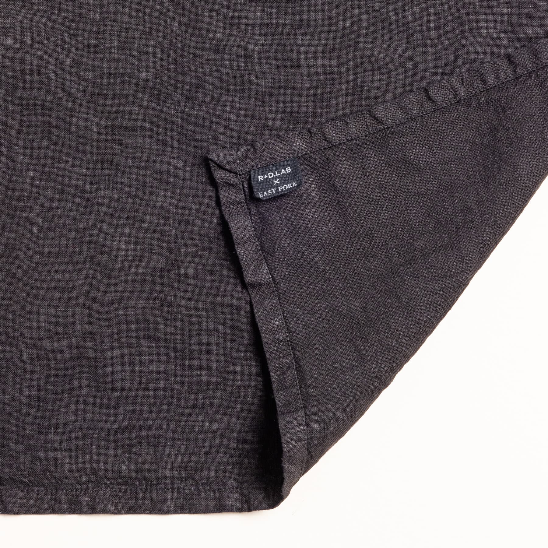 A close up of a corner of a black linen napkin with a tag that reads 'R+D Lab x East Fork'