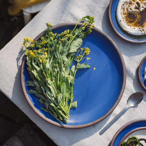 Simple wildflowers are sitting on a large ceramic serving platter in a cobalt blue color with an unglazed rim.