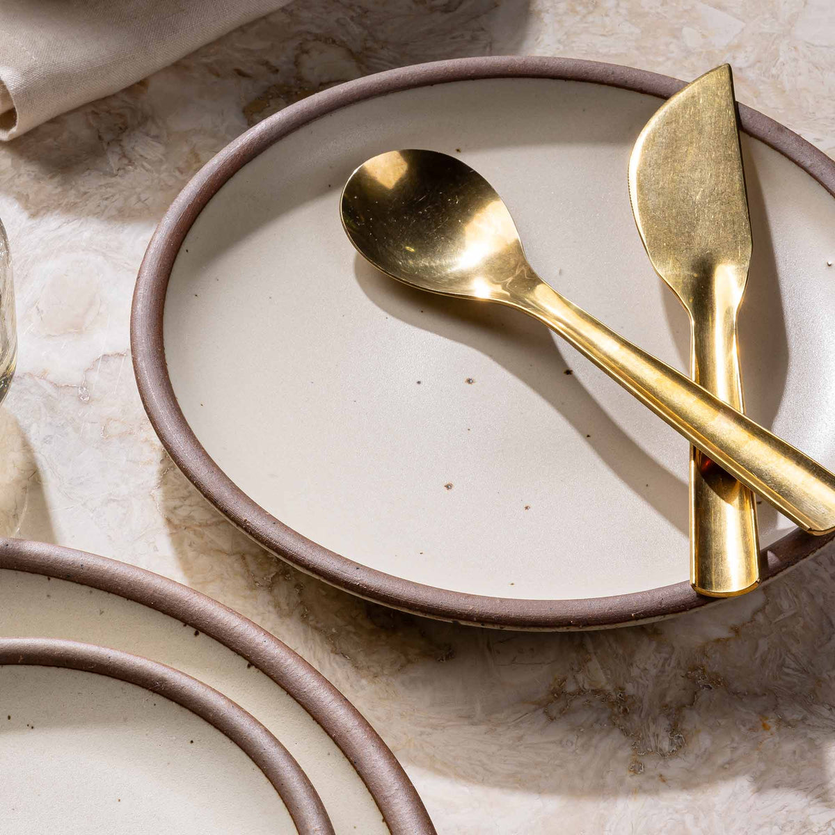 Ceramic cream plate with unglazed rim with brass flatware sitting on top.