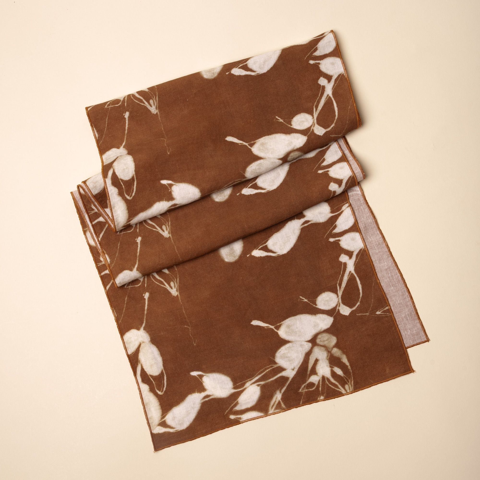 Brown linen table runner with white botanical print, folded neatly on a neutral background.