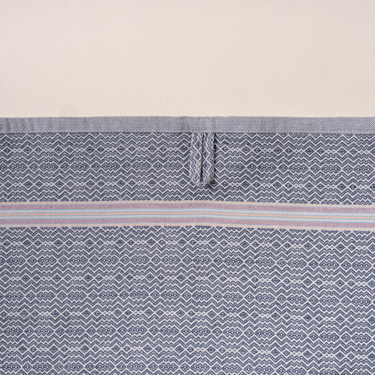 Close-up of a grey woven towel with a zigzag-and-diamond texture, stitched hanging loop, and thin striped band detail.